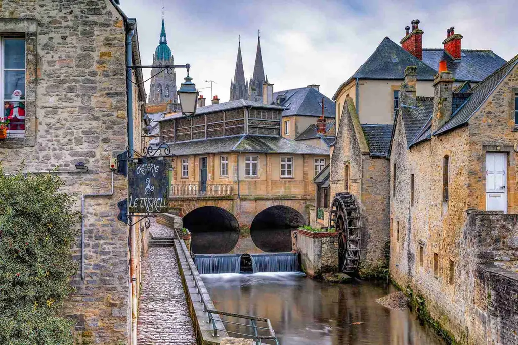Le vieux moulin et sa roue à aubes sur l’Aure à Bayeux, les flèches de la cathédrale en arrière-plan