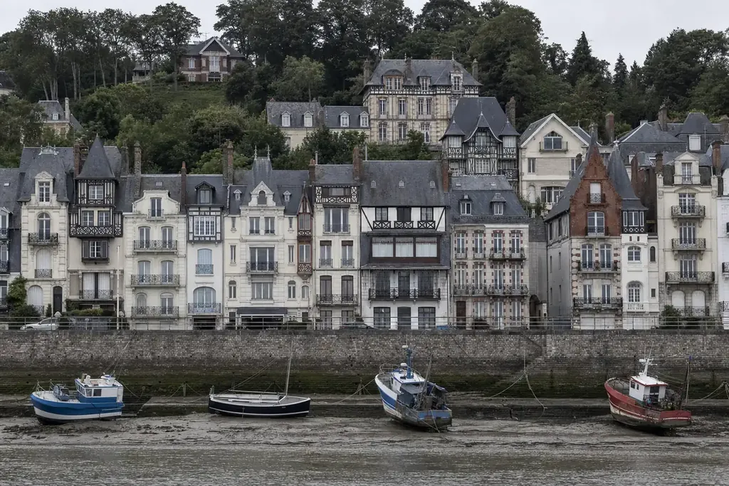 Façades balnéaires en brique et pan de bois alignées le long d’un quai, bateaux de pêche échoués à marée basse